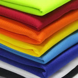 A stack of brightly colored fabrics in neon green, red, orange, yellow, blue, purple, and white, showcasing varied textures.