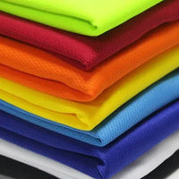 A stack of vibrant, folded fabrics showcasing colors: neon green, red, orange, yellow, light blue, dark blue, and white.