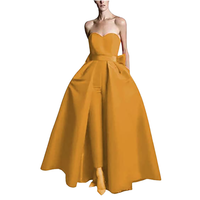A strapless golden gown with a fitted bodice flares into a voluminous skirt. The design exudes elegance and sophistication, with hands in pockets.