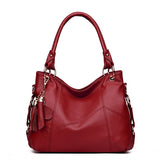 A stylish red leather handbag with a soft silhouette, featuring decorative tassels and silver hardware details.
