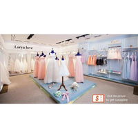 Bridal shop display featuring pastel pink and white dresses on mannequins. Light blue walls with more dresses on racks. Elegant, serene atmosphere.
