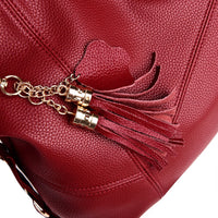 Close-up of a rich red leather handbag featuring a decorative tassel and a gold chain accent, highlighting its textured surface.