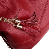 Close-up of a rich red leather handbag featuring a decorative tassel and a gold chain accent, highlighting its textured surface.
