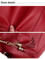 Close-up of rich red textured leather, showcasing a finger pressing into its surface and decorative tassels with gold hardware.