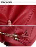 Close-up of rich red textured leather, showcasing a finger pressing into its surface and decorative tassels with gold hardware.