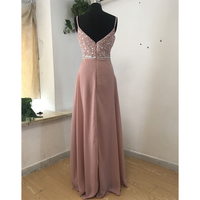 Elegant pink evening gown on a mannequin, featuring a sequined bodice with thin straps and a flowing skirt. The setting is a simple room with plants.