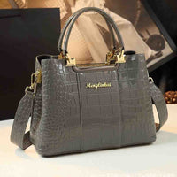 Stylish grey handbag with a crocodile texture, gold accents, and a detachable shoulder strap, showcasing elegance and functionality.