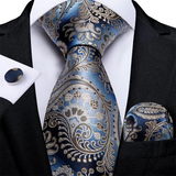Blue and silver paisley tie set with matching pocket square and cufflinks on a black suit.