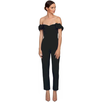 Woman in a black, off-the-shoulder jumpsuit with ruffled sleeves and fitted pant legs. She stands confidently, looking to the side against a white background.