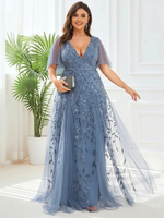 A woman in a blue, beaded evening gown stands gracefully, holding a clutch. The room is elegant, featuring white walls and a potted plant. She smiles warmly.
