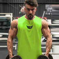 A muscular individual wearing a bright green sleeveless top holds a dumbbell in each hand while posing in a gym setting.