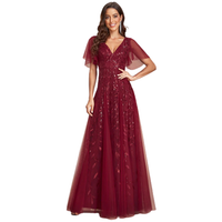 A woman wearing a deep red gown with sheer, flowing sleeves and floral lace details smiles confidently. The dress conveys elegance and grace.