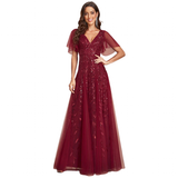 A woman wearing a deep red gown with sheer, flowing sleeves and floral lace details smiles confidently. The dress conveys elegance and grace.