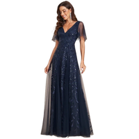 Woman wearing a navy blue evening gown with sheer sleeves and embroidered details. She smiles softly, exuding elegance and confidence against a plain background.