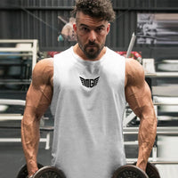 A muscular individual in a sleeveless white gym shirt holds two heavy dumbbells, showcasing impressive biceps in a fitness center.