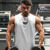 A muscular individual in a sleeveless white gym shirt holds two heavy dumbbells, showcasing impressive biceps in a fitness center.