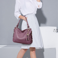 A woman in a white blouse and light gray skirt carries a stylish purple handbag with a tassel detail, set against a minimalist backdrop.