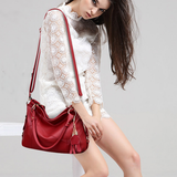 A person wearing a white lace blouse and sitting on a bench, holding a stylish red handbag with a tassel charm.