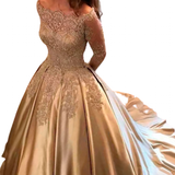 A woman in an elegant, gold gown with intricate lace details on the bodice and sleeves. The off-shoulder design and flowing skirt evoke timeless elegance.
