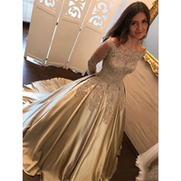 A woman wearing an elegant off-shoulder gown with intricate lace detailing and a flowing satin skirt. She smiles softly in a warmly lit room.