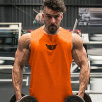 A muscular individual in an orange tank top holds dumbbells, showcasing defined arms in a gym setting with exercise equipment in the background.