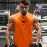 A muscular individual in an orange tank top holds dumbbells, showcasing defined arms in a gym setting with exercise equipment in the background.