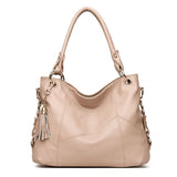 A stylish beige leather handbag with a slouchy design, featuring golden hardware and a decorative tassel charm.