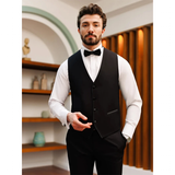 Man in a black vest and bow tie stands confidently in a stylish room with shelves and wooden paneling. His expression is calm and composed.
