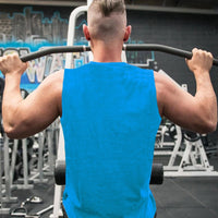 A muscular person in a blue tank top performs a pull-up in a gym, with exercise equipment and a colorful mural in the background.