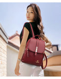 A woman in a black shirt carries a stylish burgundy backpack against a sunny backdrop of rooftops and clear blue skies.