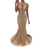 A woman is wearing a sparkling, gold, sleeveless evening gown with a keyhole neckline and a mermaid silhouette, exuding elegance and glamour.
