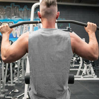 A muscular man wearing gray shirt with a short hairstyle performs a lat pull-down exercise at a gym, showcasing his toned back and arms.