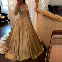 Woman in a luxurious, long-sleeved, gold ball gown with intricate lace details, poses in front of a large ornate mirror, creating an elegant atmosphere.