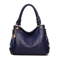 A stylish navy blue leather handbag with gold-tone accents and a tassel charm, featuring a slouchy shape and dual handles.