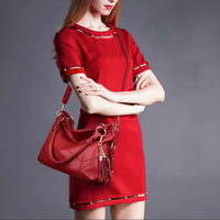Model in a stylish red dress poses with arms crossed, showcasing a matching red handbag with tassels against a gray background.