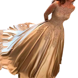 A woman in an elegant, satin gold gown with lace detailing and an off-the-shoulder neckline. The flowing skirt adds a touch of luxury and grace.