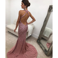 A woman wearing sparkling, backless pink gown stands in a room with a large ornate mirror. The elegant dress features a long train, and she exudes confidence.