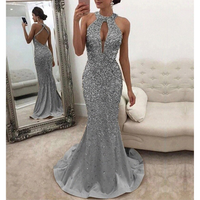 A woman wearing sparkly silver gown stands beside a mirror. The dress features a keyhole neckline and open back. Elegant and glamorous setting.