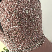 Close-up of a pink dress adorned with intricate beadwork and sequins, showcasing elegance and luxury. The details sparkle in soft light.