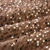Close-up of gold sequins on beige fabric, creating a shimmering, luxurious pattern. The fabric appears soft and has a slightly wavy texture.