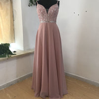 Elegant pink gown on a mannequin, featuring a sparkly beaded bodice with thin straps and a flowing A-line skirt. Soft and graceful setting.