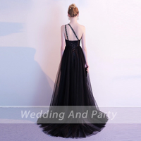 A woman in a black evening gown with a single studded strap poses against a light background. The gown has a long flowy train, creating an elegant, sophisticated look.