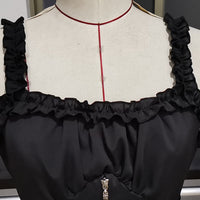Close-up of a black ruffled top on a dress form. The top features ruched straps and a front zipper, conveying a stylish and elegant design.