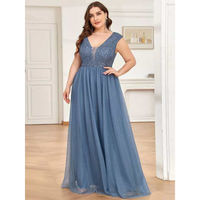 A woman in a blue evening gown with a sequined bodice stands confidently on a wooden floor in a bright room, conveying elegance and grace.