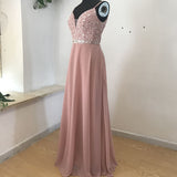 A mannequin displays a sleeveless, floor-length pink gown. The bodice is sequined, with a deep V-neck and a sparkly waistband. Soft, elegant setting.