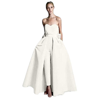 A woman wearing a strapless white gown featuring a fitted bodice, flowy overskirt, and sleek pants. The look is elegant and modern.