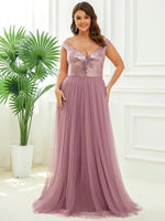 Woman in a mauve evening gown with a sequin bodice smiles in a bright room. The dress flows elegantly, and a potted plant is in the background.