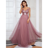 Woman in an elegant mauve gown with sequined bodice and flowing tulle skirt stands in front of a white-paned window, exuding grace and confidence.
