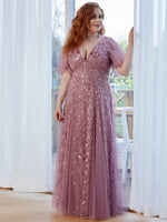A woman wearing an elegant mauve gown with leaf patterns. She appears serene and content, with natural light filtering in.