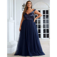 Woman in an elegant, navy blue evening gown with sequined top and flowing tulle skirt, standing confidently by white French doors.